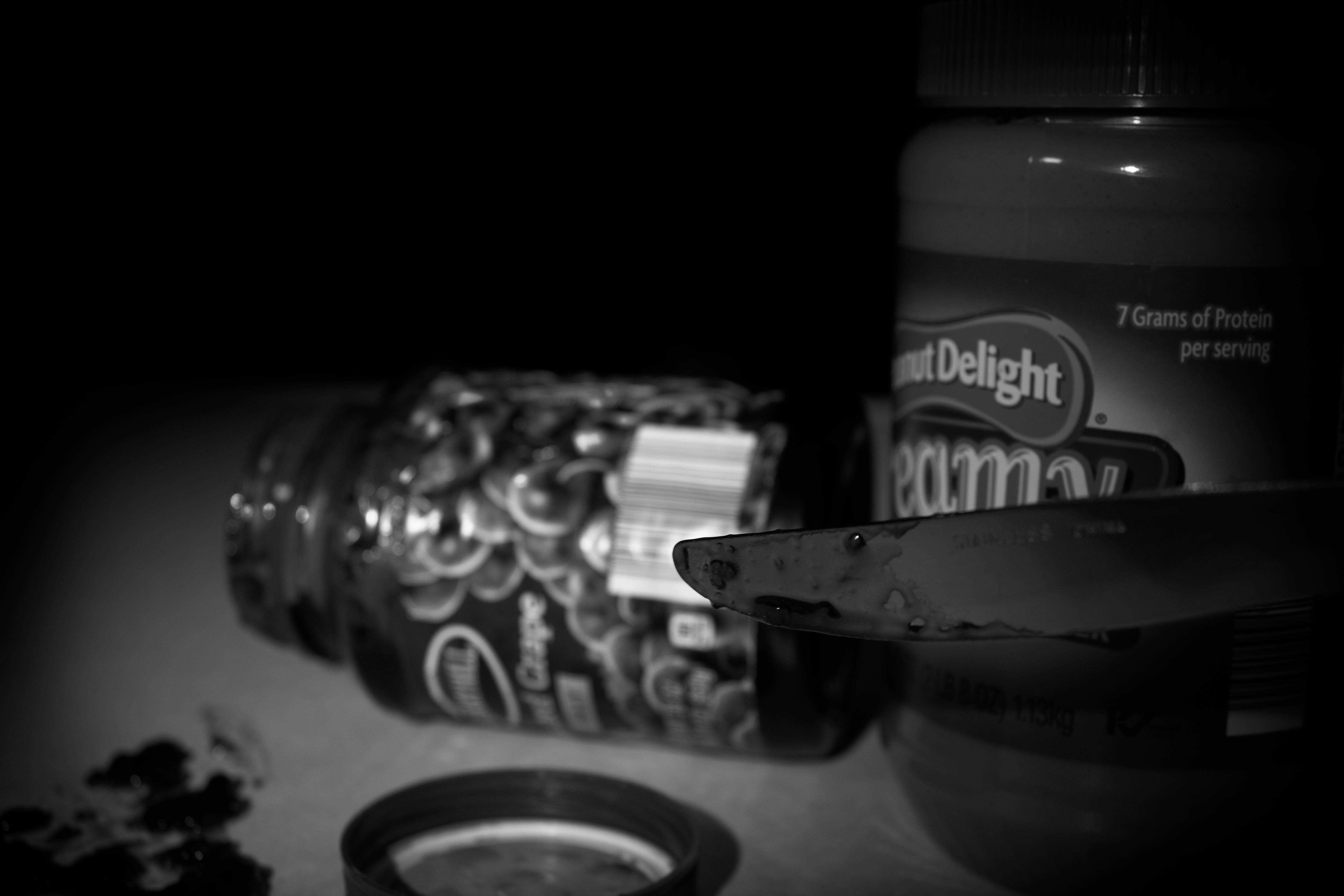 Peanut butter looming over jelly with knife.